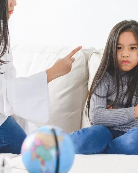 Angry asian mother sitting with little daughter , mom scolds for