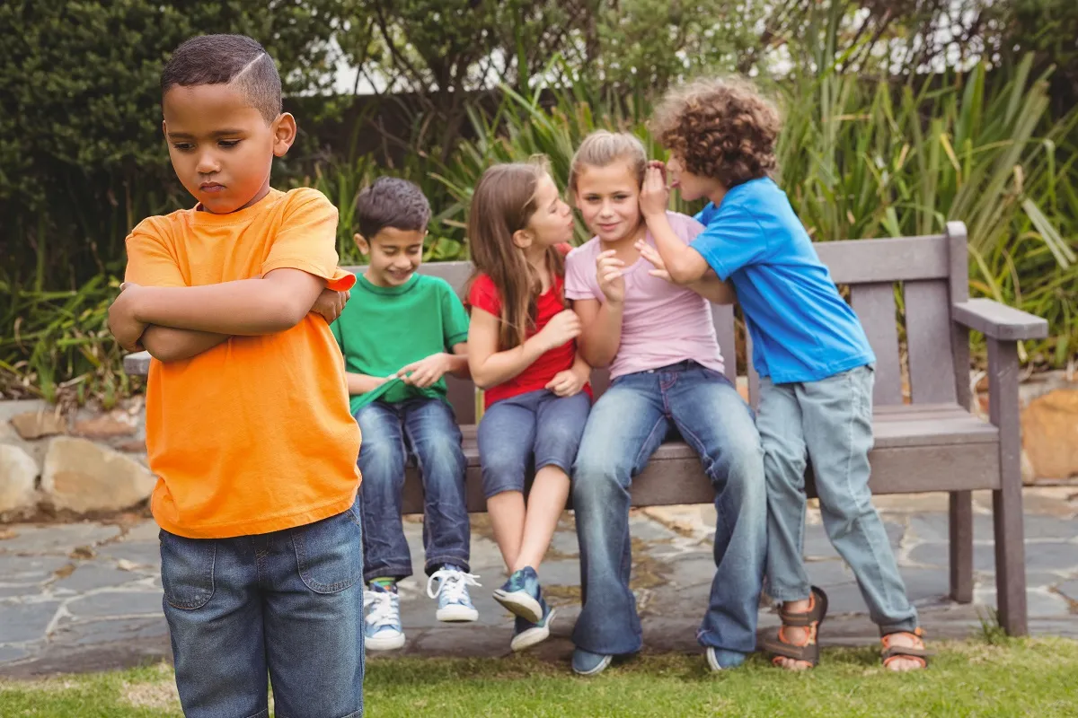 Upset child standing away from group sitting on a bench