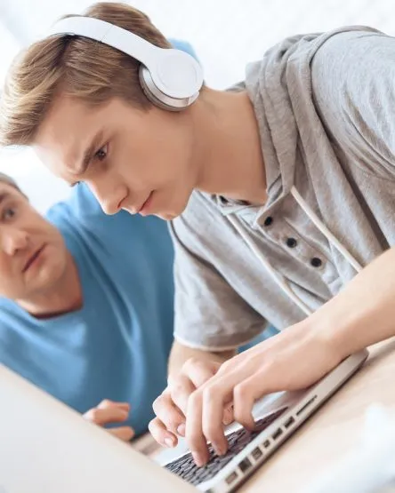 Son is playing on laptop. Father tries to talk to troubled teenager.