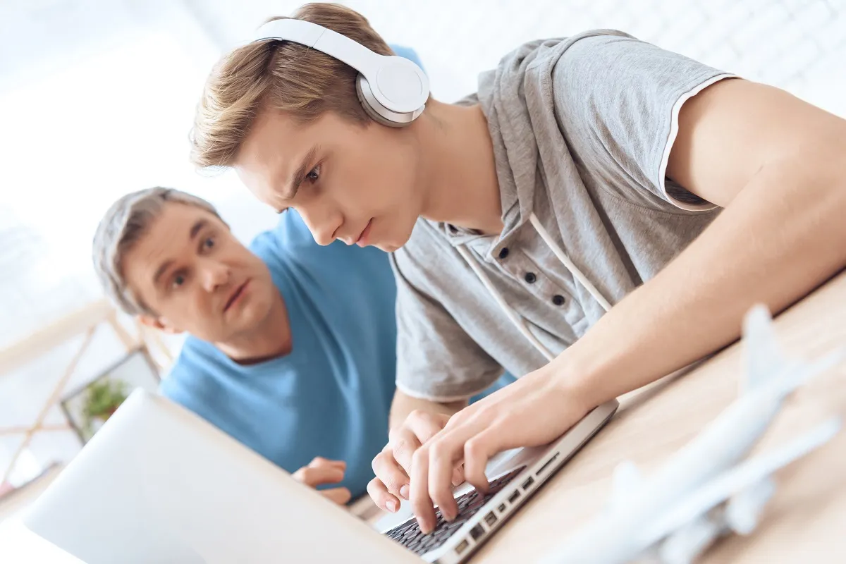 Son is playing on laptop. Father tries to talk to troubled teenager.