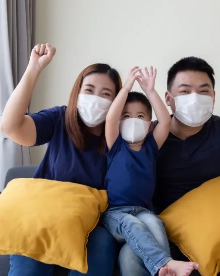 Asian family wearing protective medical mask for prevent virus Covid-19 and hand up and sitting together in living room. Family protection from contaminated air concept