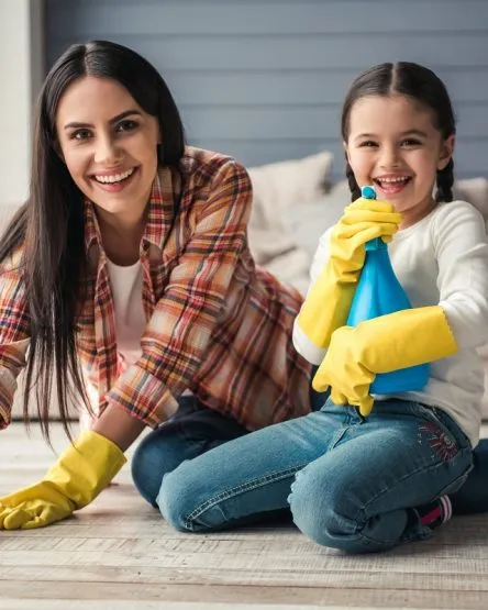 Woman and her daughter are smiling while cleaning floor.