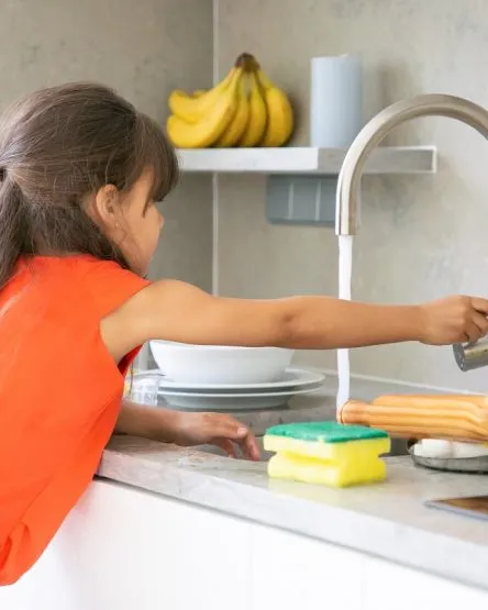 Cute little girl washing dish in kitchen by herself