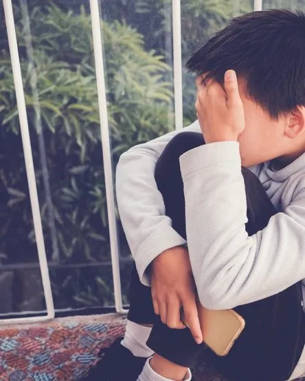 Young Asian preteen teenager boy hugging his knee and cover his