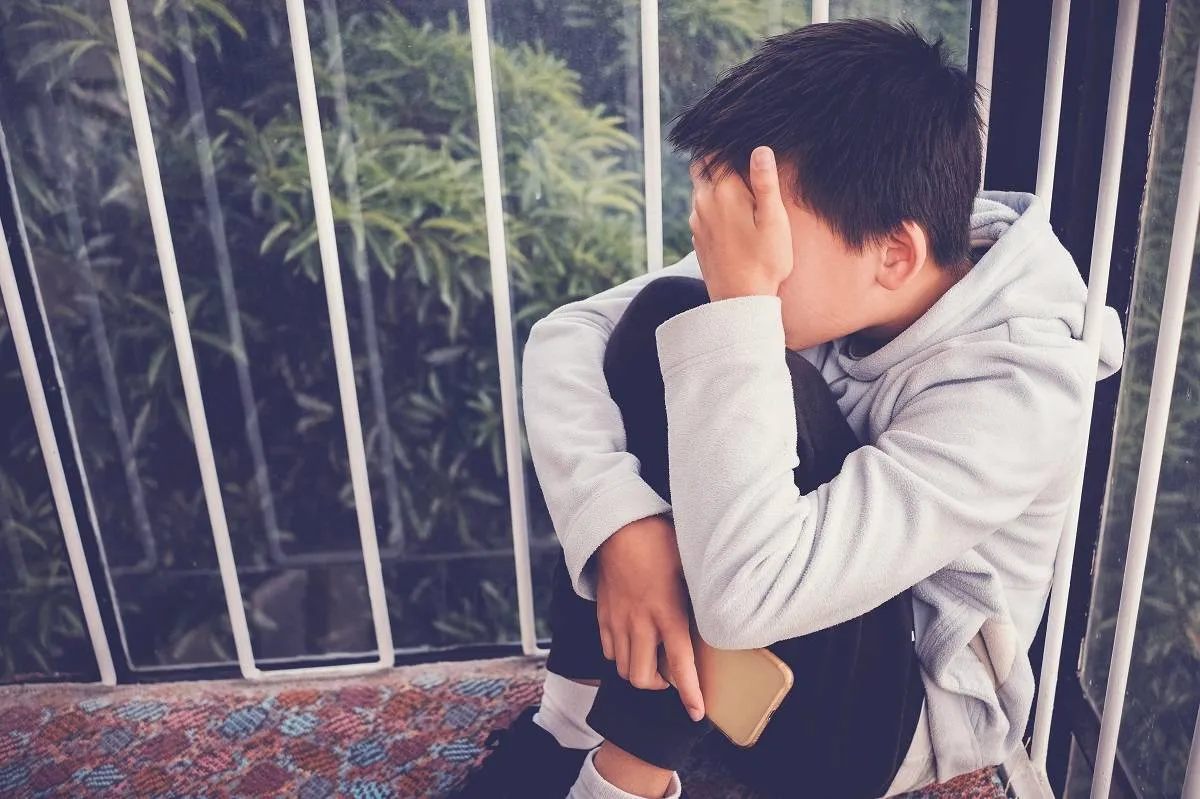 Young Asian preteen teenager boy hugging his knee and cover his