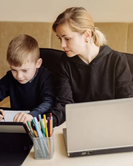 Mother using laptop and tablet teaching with her son online at home in his room