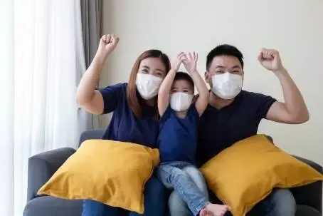 Asian family wearing protective medical mask for prevent virus Covid-19 and hand up and sitting together in living room. Family protection from contaminated air concept