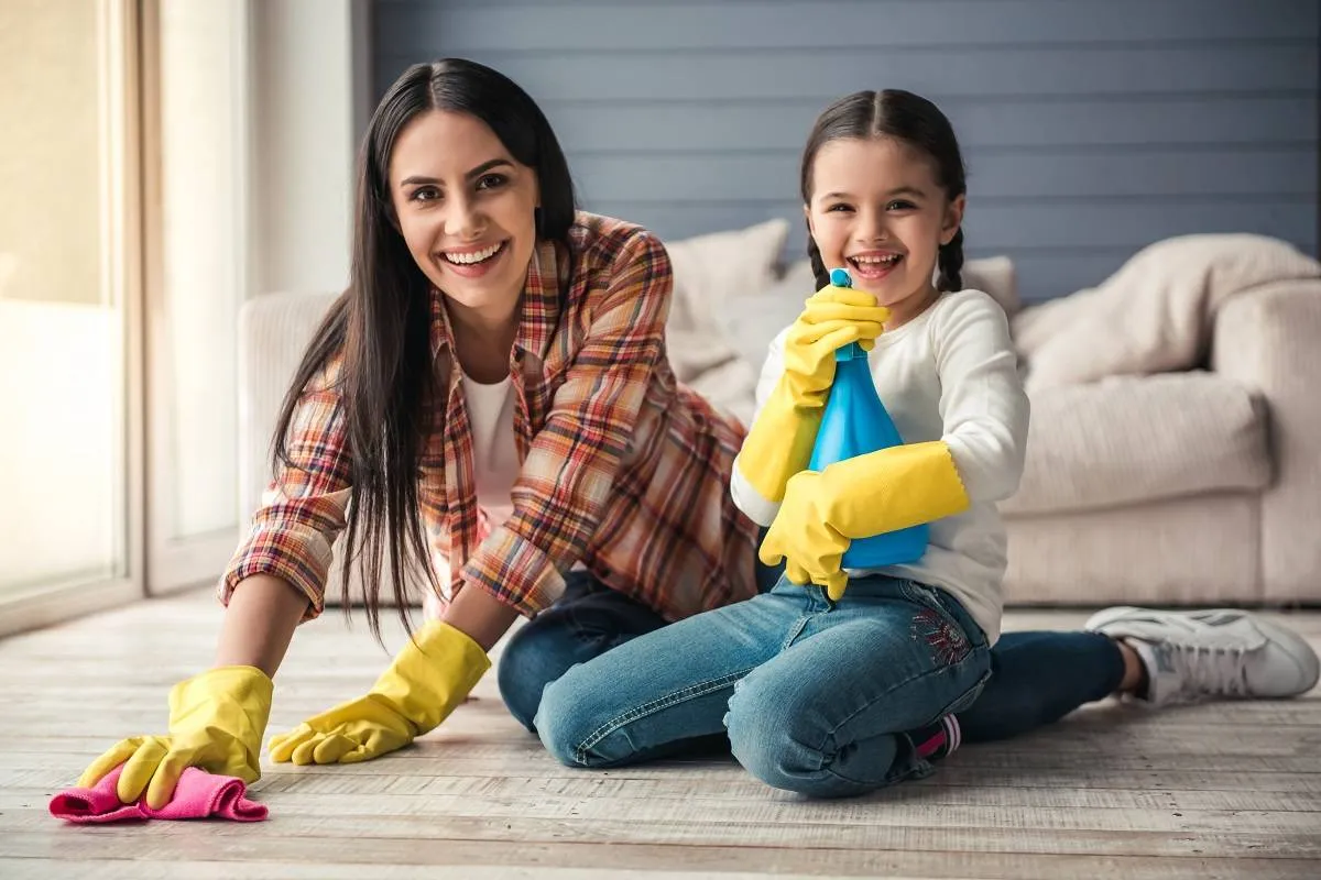 Woman and her daughter are smiling while cleaning floor.