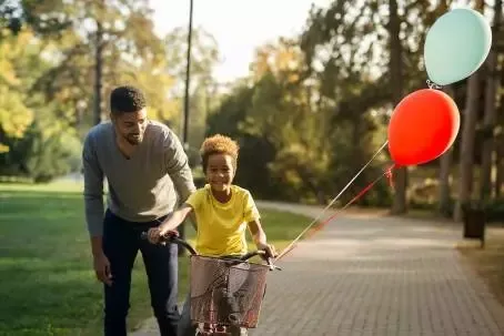 Happy father teaching his cute daughter to ride a bicycle in park.