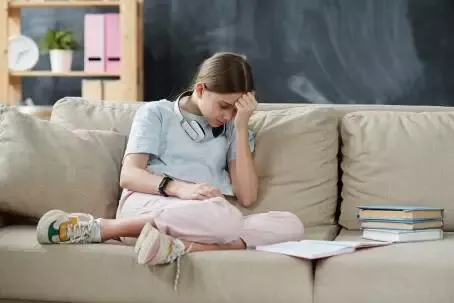 Sad teenage girl with books being upset because of self isolation at home
